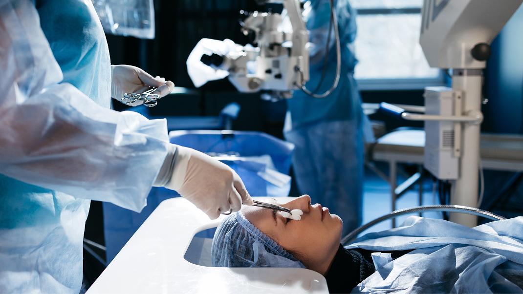 Preparazione di una procedura oculistica in ambiente sterile. Il paziente è posizionato sul lettino mentre il personale sanitario utilizza strumenti specialistici per il trattamento di patologie retiniche, come l'edema maculare diabetico o la degenerazione maculare.