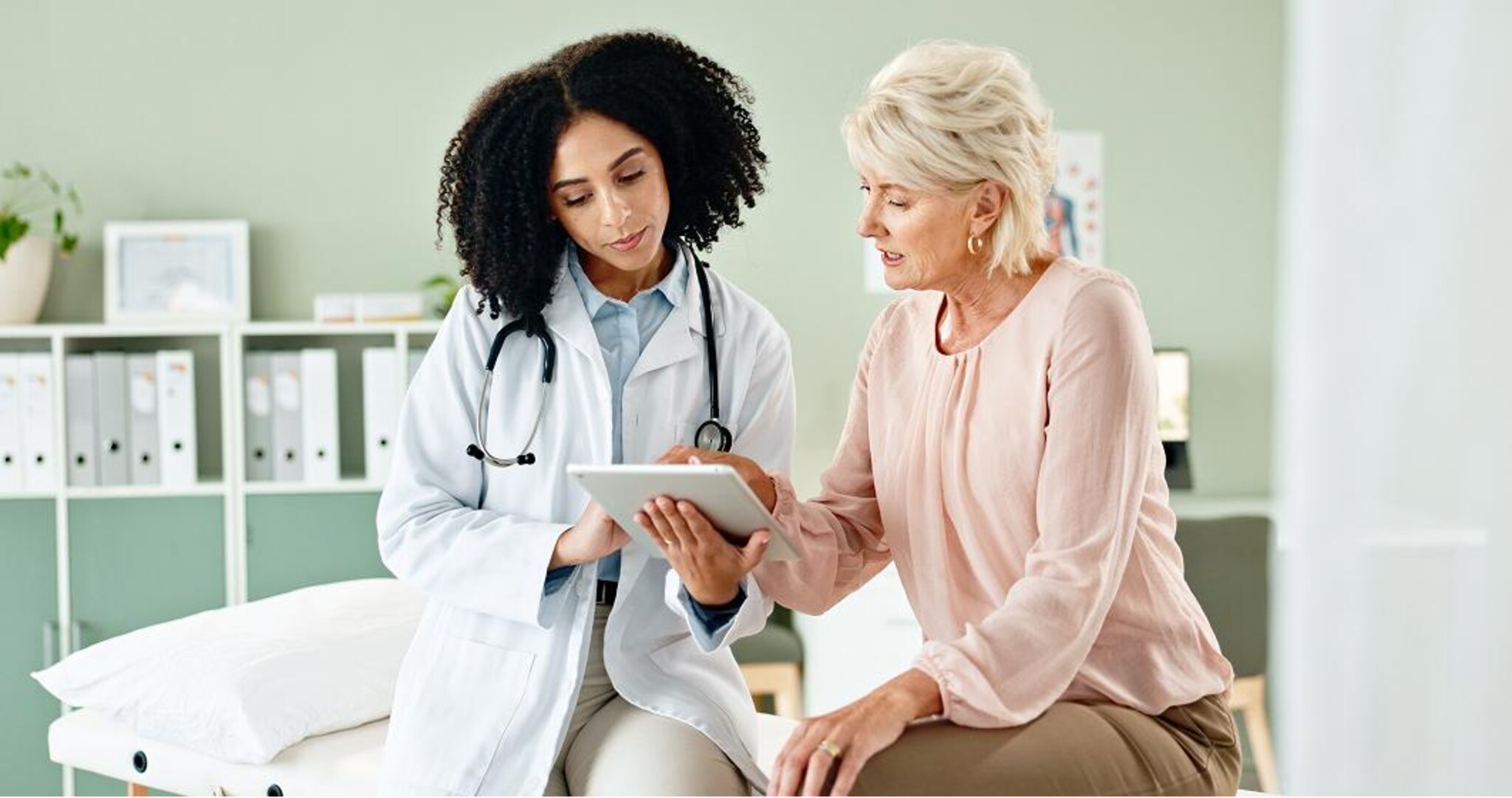 Professionista sanitario e persona assistita consultano informazioni sanitarie su un tablet durante una visita.