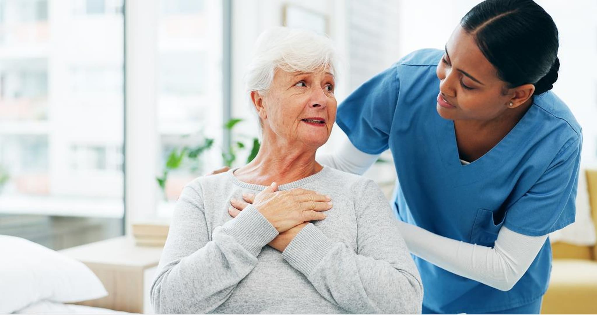 Persona anziana con entrambe le mani sul petto assistita da un professionista sanitario.