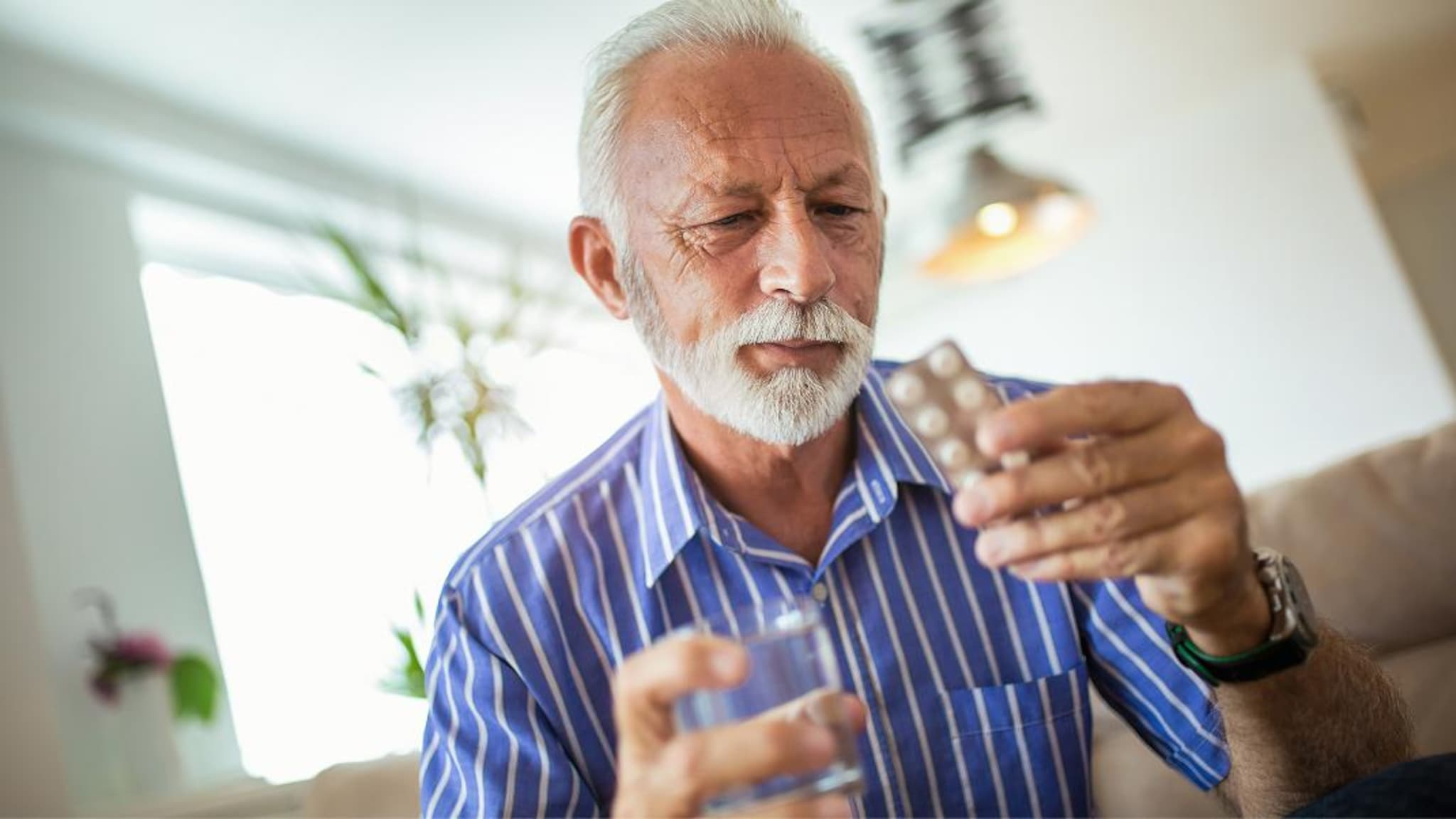 Persona osserva una confezione di farmaci e un bicchiere d'acqua prima dell'assunzione della terapia.