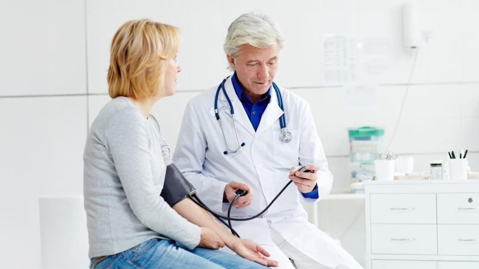 Professionista sanitario che misura la pressione arteriosa a una persona seduta, con bracciale applicato al braccio.
