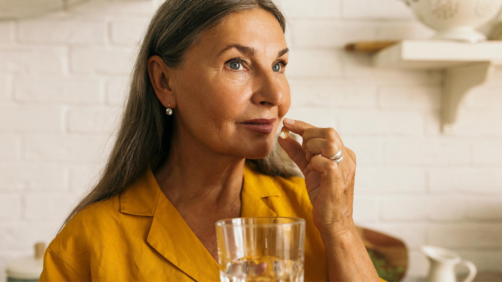 Persona adulta nell'atto di assumere una capsula, tenendola vicino alla bocca, con un bicchiere d'acqua in primo piano.