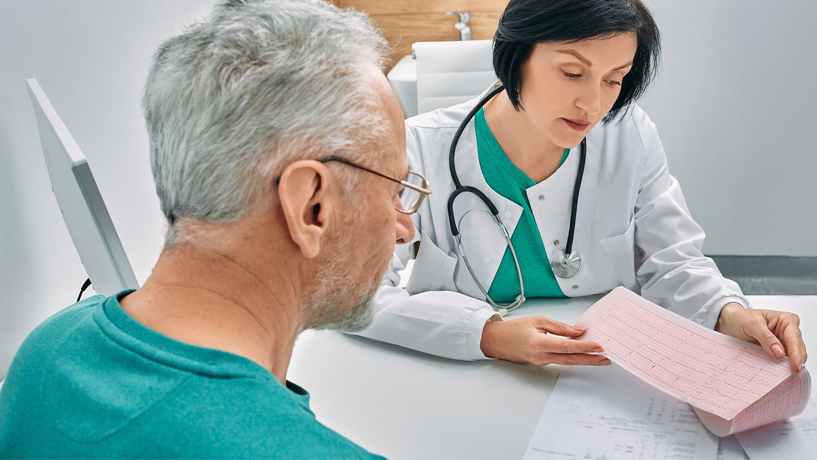 Professionista sanitario mostra e discute con una persona adulta un elettrocardiogramma stampato durante una visita.