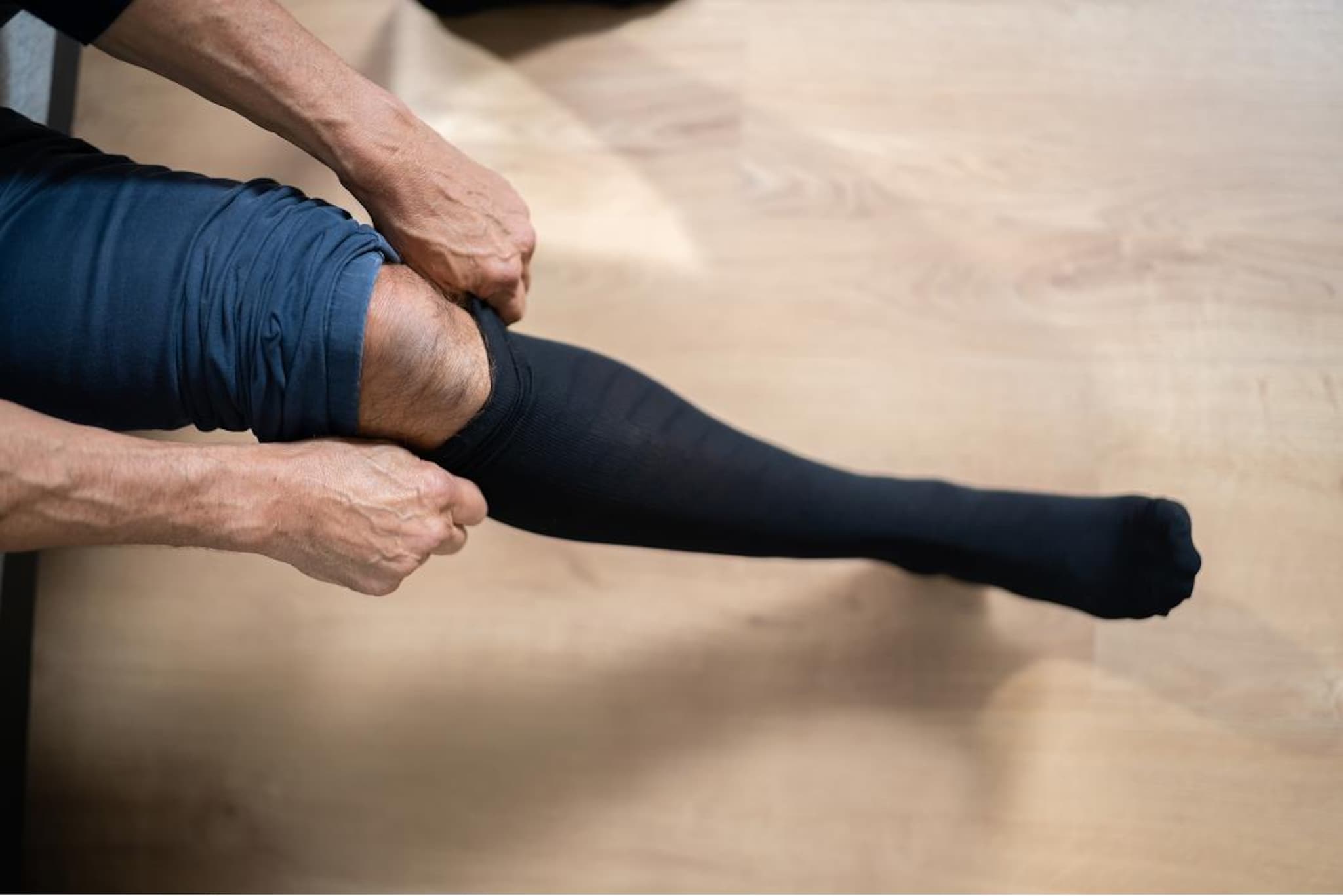 Persona seduta che tiene una gamba sollevata e indossa una calza compressiva scura fino alla coscia, sistemandone il bordo con le mani.