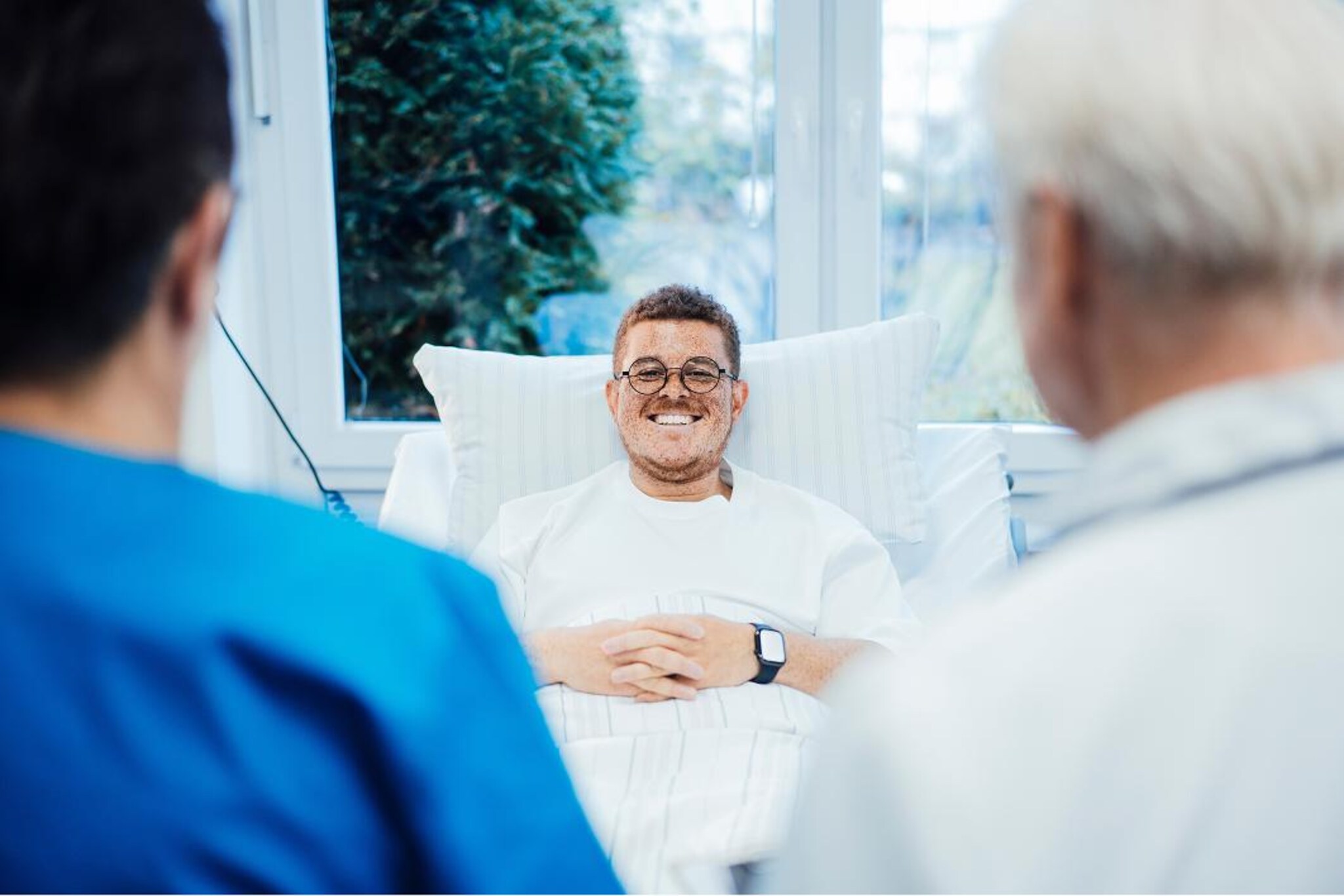 Persona distesa in un letto ospedaliero durante un colloquio con due membri del personale sanitario visibili in primo piano.
