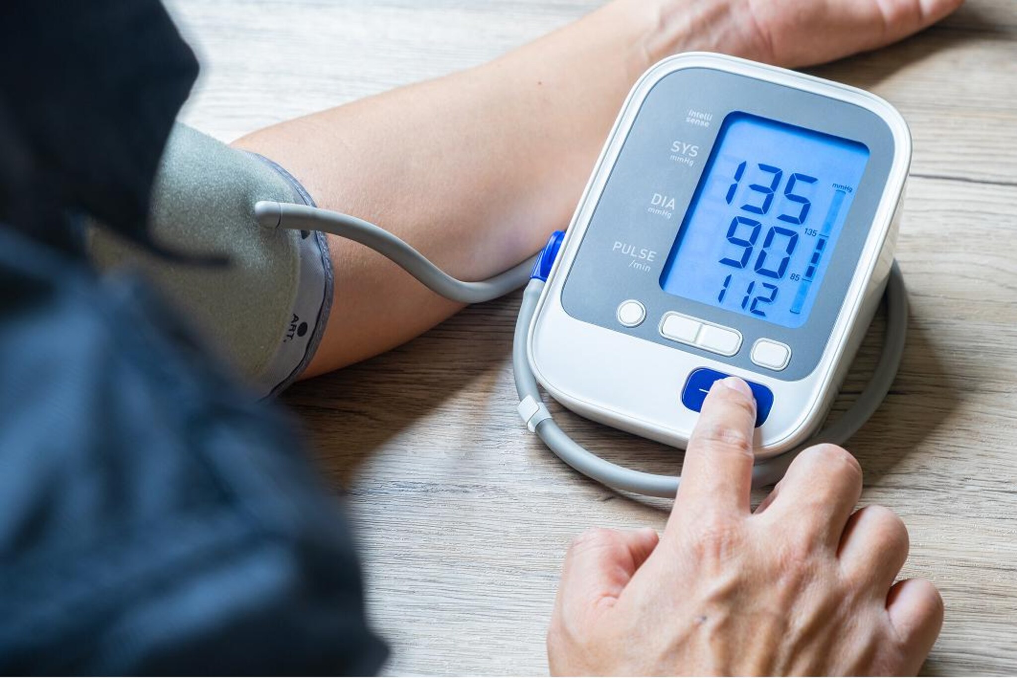 Primo piano di un misuratore digitale della pressione collegato al bracciale applicato al braccio di una persona, con valori 135/90 mmHg e frequenza cardiaca di 112 battiti al minuto sul display.