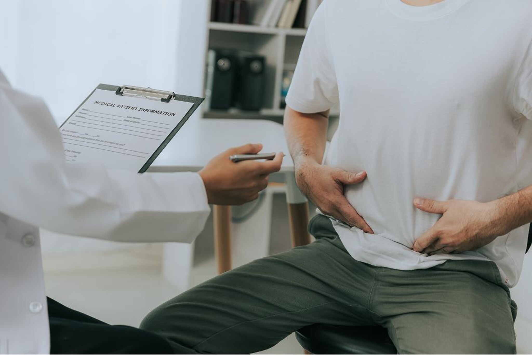Persona durante un consulto medico indica dolore o disagio nella zona addominale.